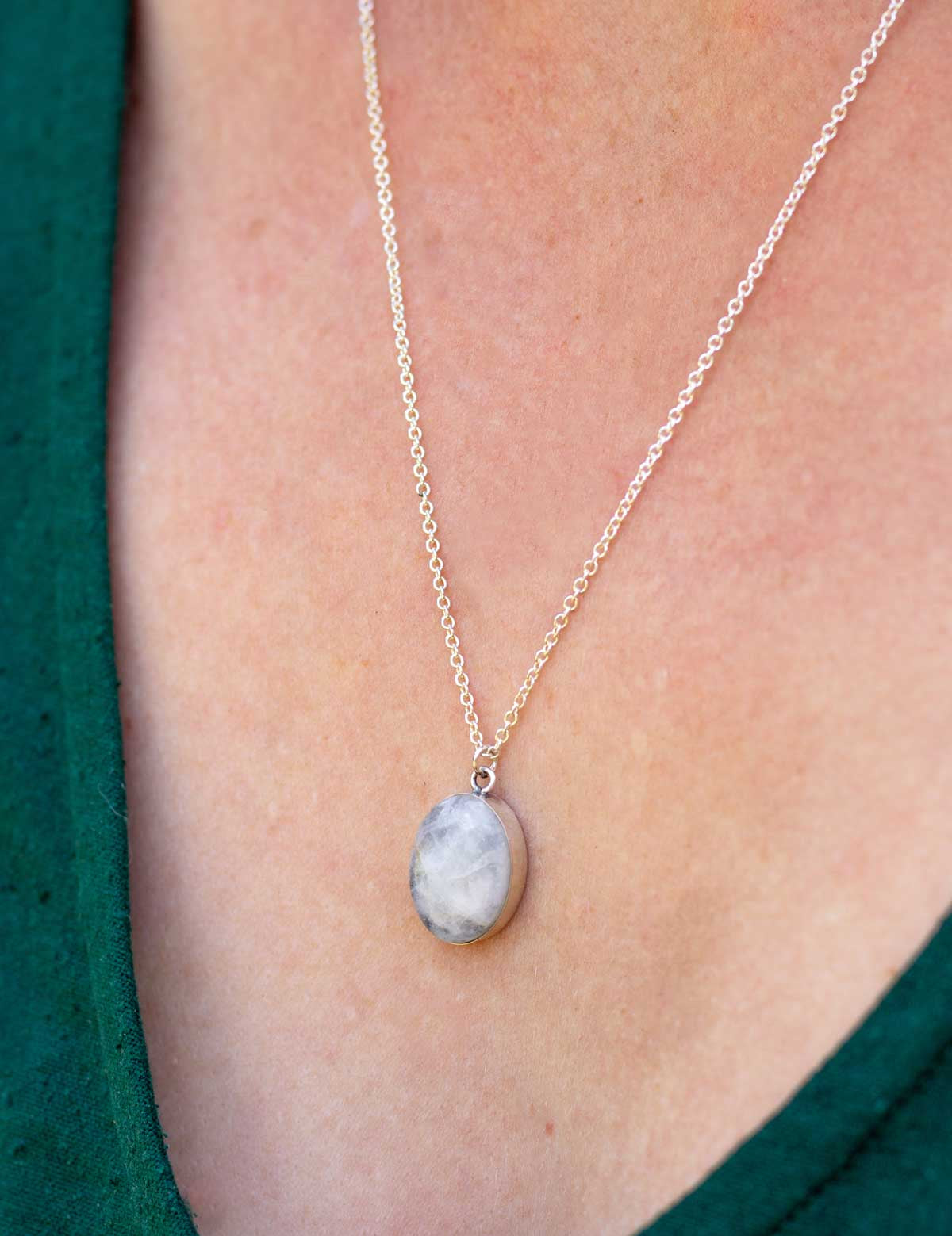 Silver chain necklace with an oval pendant made from natural white stone, worn on a person in a green dress