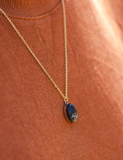 14k gold fill necklace with an oval black stone pendant worn by a person in an orange shirt