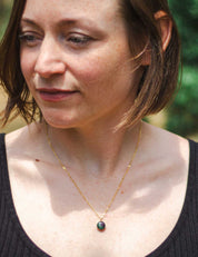 A woman with short hair wears a custom gold necklace made from natural rock set into a small round pendant
