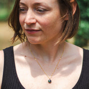 A woman with short hair wears a custom gold necklace made from natural rock set into a small round pendant
