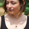 A woman with short hair wears a custom gold necklace made from natural rock set into a small round pendant