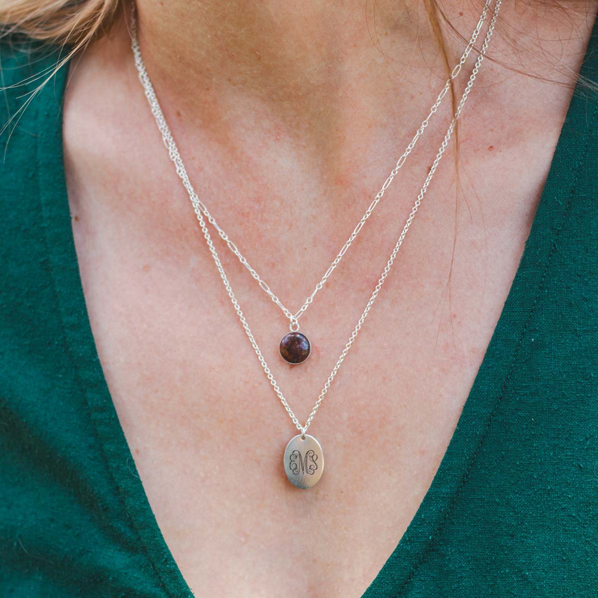 A woman wears a sterling silver charm necklace personalized with her name as an engraved monogram