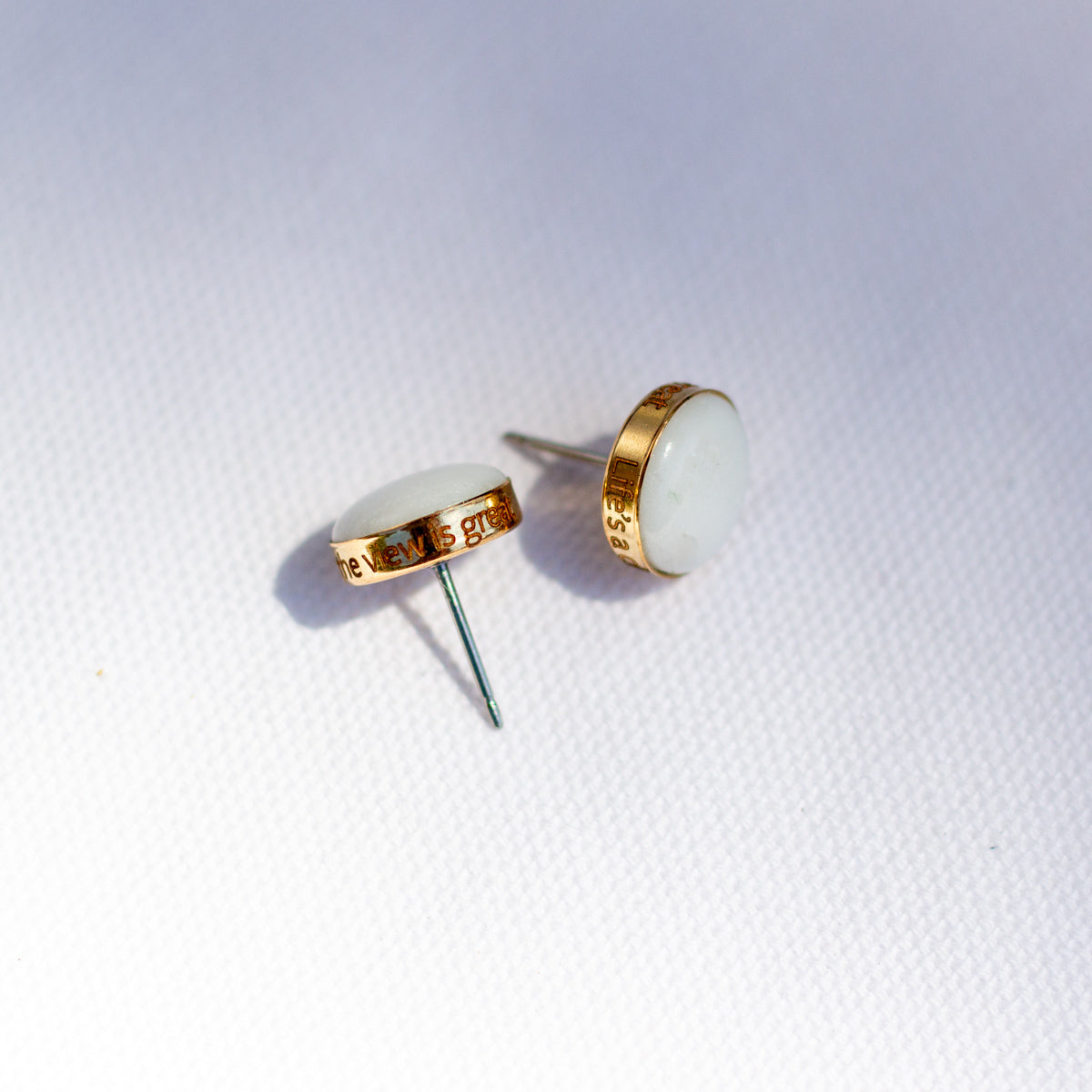 A pair of white stud earrings with a stone set in a 14k gold fill cup. The edge is personalized with custom engraving.