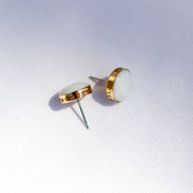 A pair of white stud earrings with a stone set in a 14k gold fill cup. The edge is personalized with custom engraving.