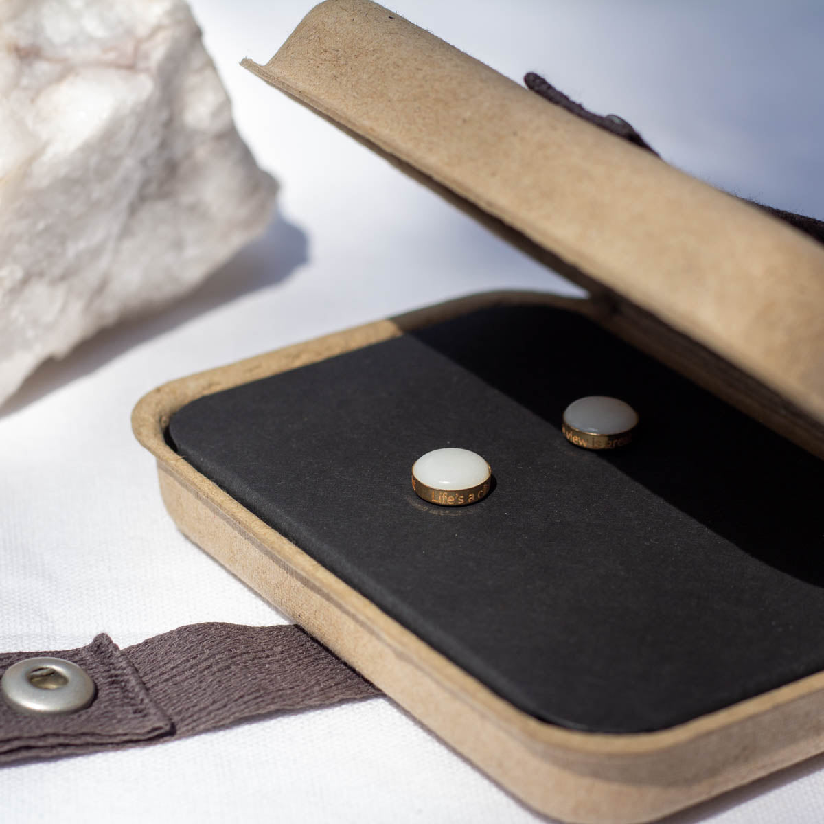 A pair of white stone earrings made from natural stone and engraved on the edge. They sit in a kraft gift box.