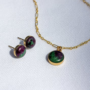 Gold stone pendant necklace with matching purple and green stone stud earrings on a white background