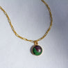 Close-up shot of a speckled purple and green rock set as a small round charm and hung on a 14k gold chain