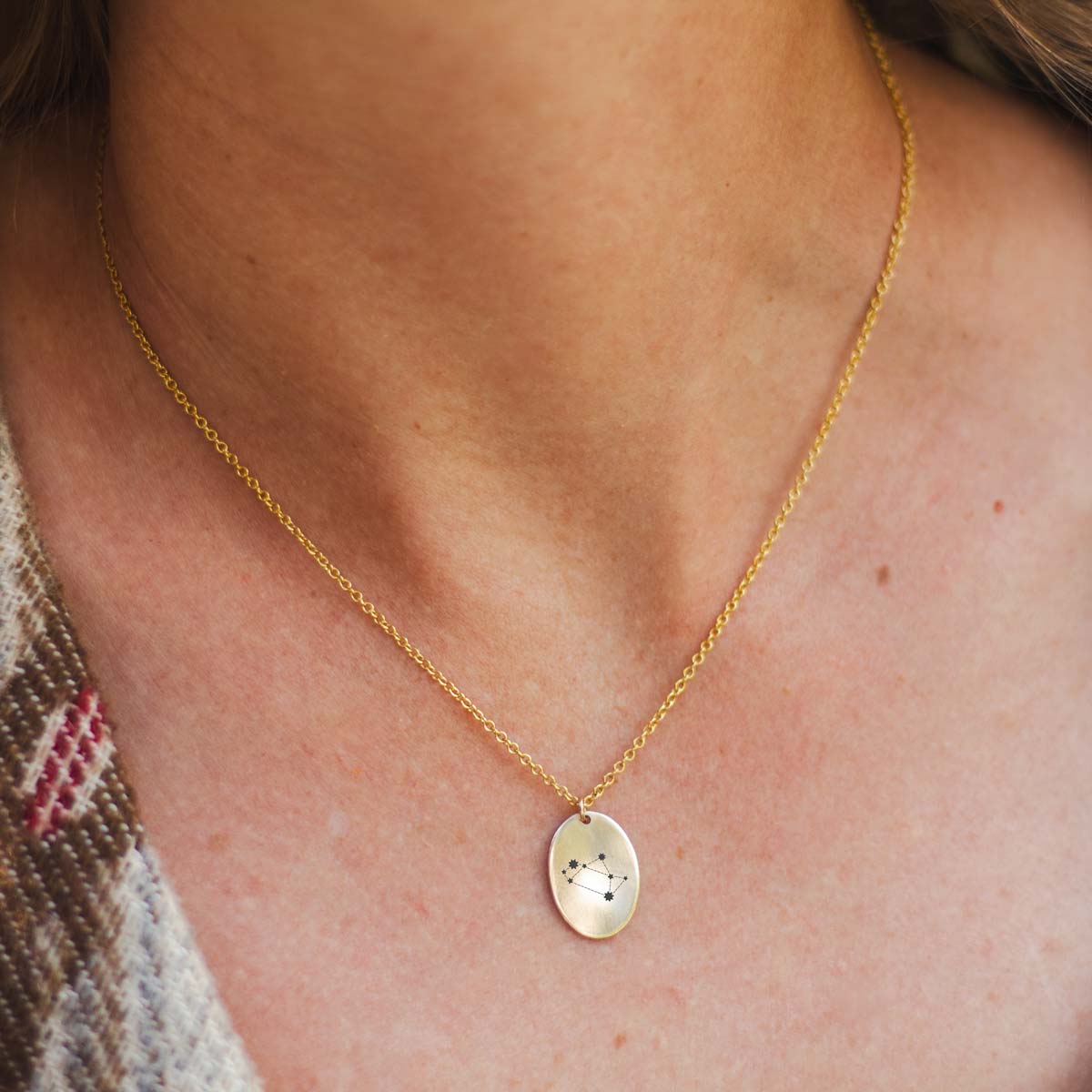 A woman wearing a 14k gold fill charm necklace engraved with a zodiac sign