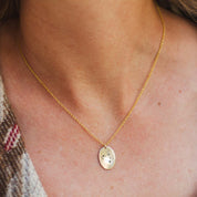 A woman wearing a 14k gold fill charm necklace engraved with a zodiac sign