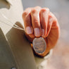 Woman holding engraved silver pendant necklace that reads, "How wild it was to let it be." by Cheryl Strayed