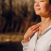 A woman wears layered stone pendant and engraved voyager charm necklaces