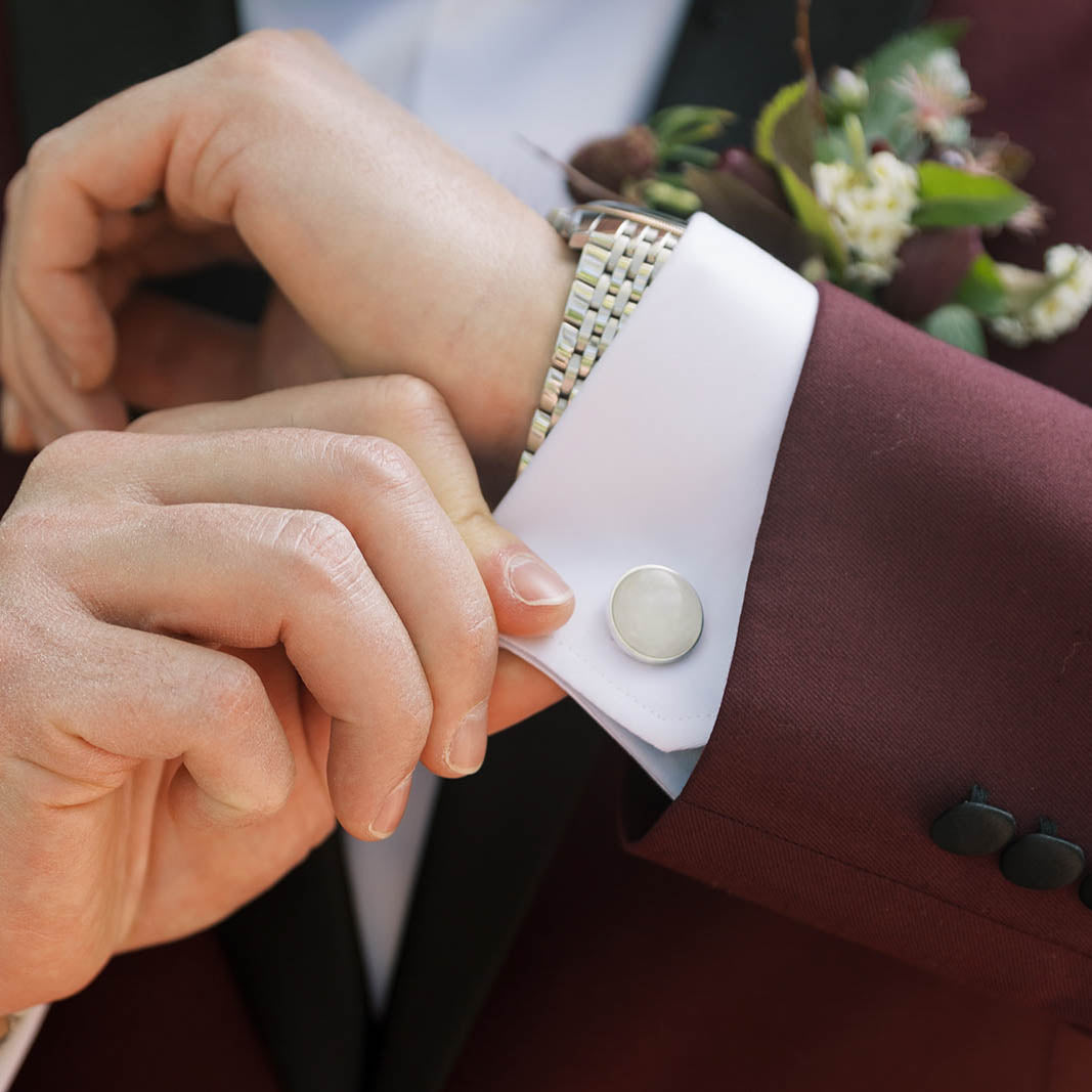 A groom in a burgundy suit wears French cuffs with sterling silver cufflinks set with pure white marble from Colorado