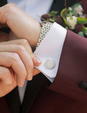 A groom in a burgundy suit wears French cuffs with sterling silver cufflinks set with pure white marble from Colorado