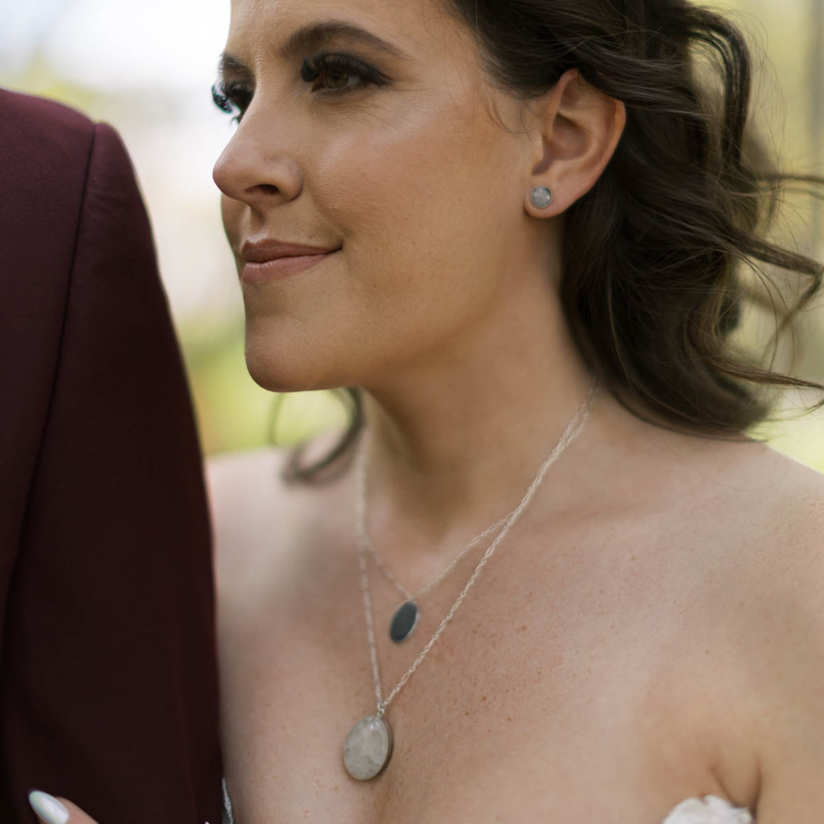 A bride wearing matching jewelry including natural stone earrings, a pendant necklace, and a layered silver charm necklace
