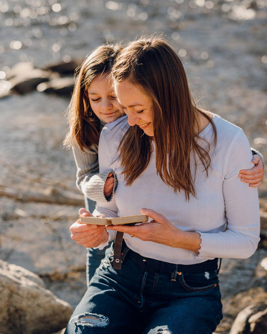 A mother holds an open jewelry gift box while her child hugs her from behind