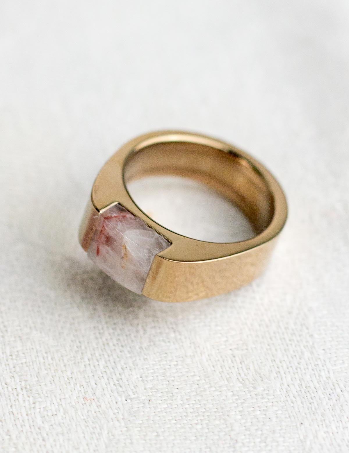 A pink quartz rock inset into a chunky champagne color stainless steel ring
