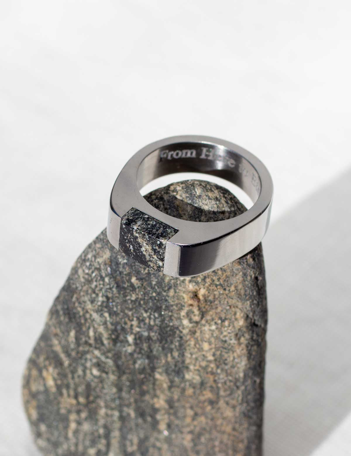 Engraved silver stainless steel signet ring set with natural granite sitting on the rock it was made from