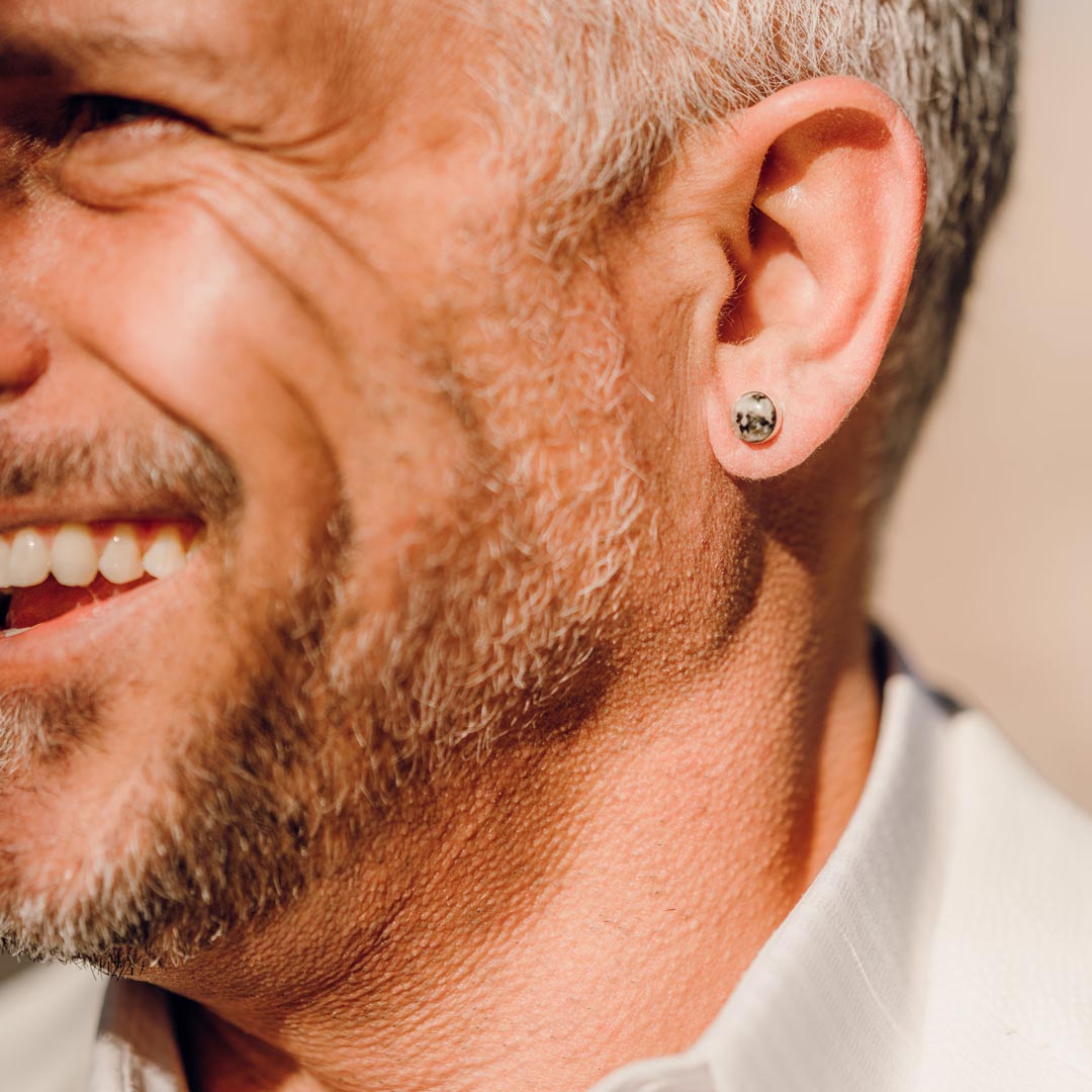 A smiling man wearing small stone stud earrings
