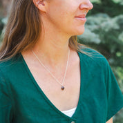 Styled shot of our founder Leslie wearing a necklace with a small, round stone charm. She's paired it with a me-made green dress.