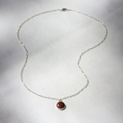 A small, round charm set with fossilized dinosaur bone hangs from a long/short sterling silver chain