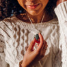 Woman holding a beautiful blue-green stone pendant necklace while wearing it over a white sweater
