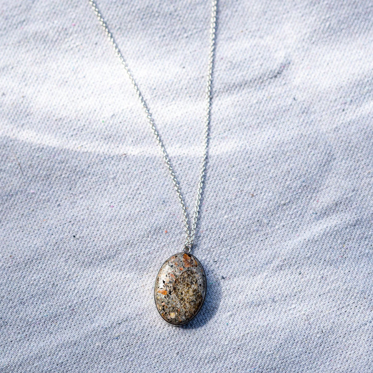 A long pendant necklace on a sterling silver chain made of an oval shaped piece of cement
