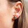 Woman wearing round stud earrings made of a speckled black and white stone
