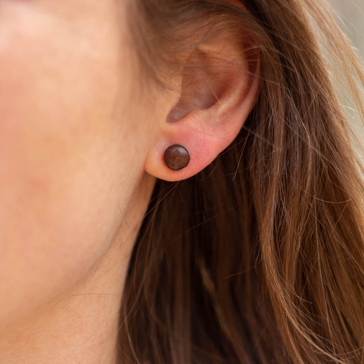Woman wears small round stone earrings made of reddish-brown rock